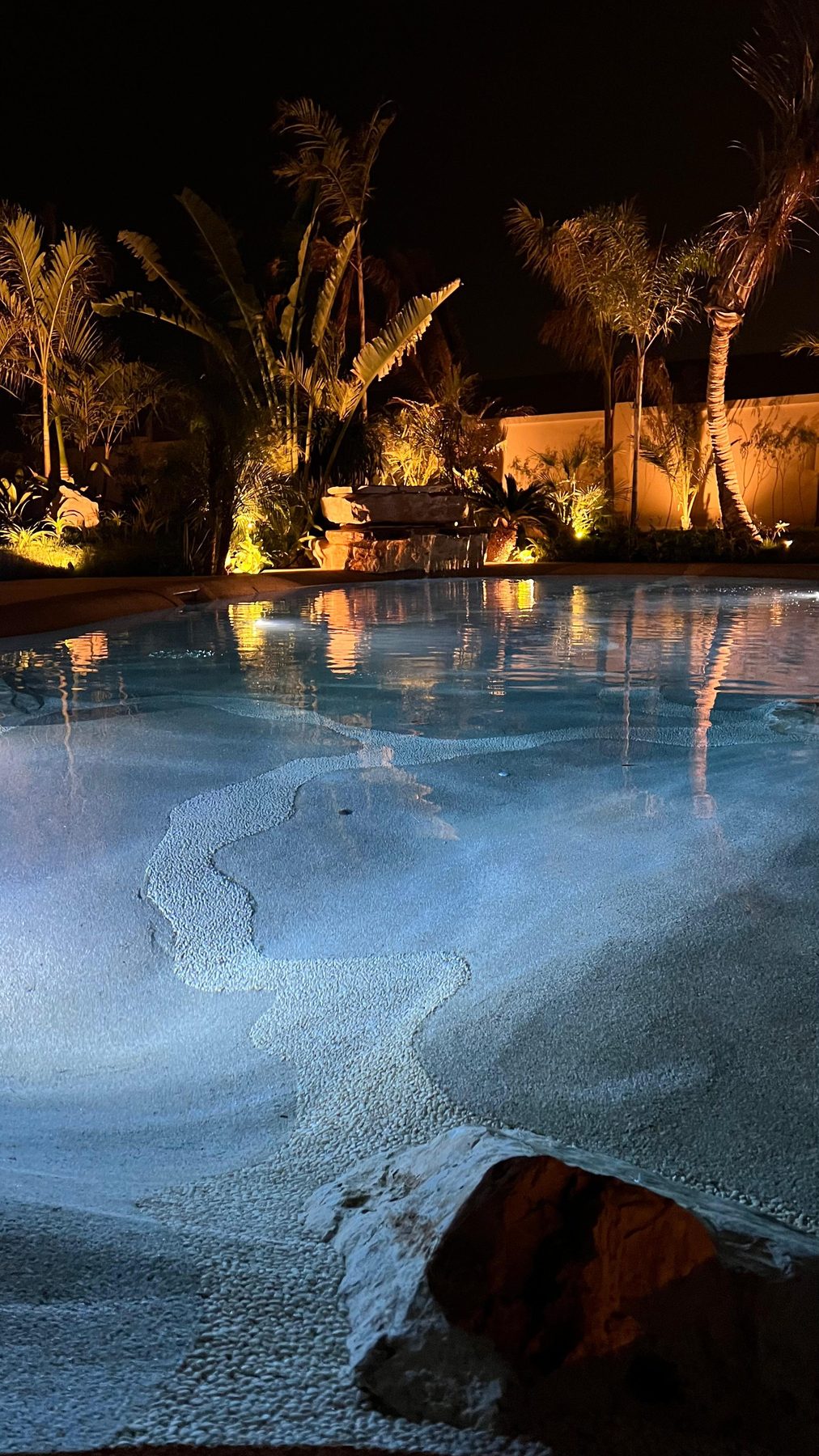 A natural beach-entry pool at dusk with a sandy gradient shoreline, turquoise water and palms — an Abu Dhabi project by LEGO Design